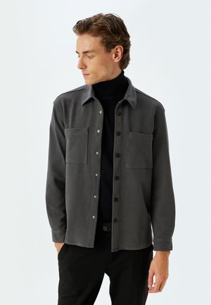 Donkergrijze shirtjas van textuurstof, met twee borstzakken, een knoopsluiting aan de voorkant en een standaardkraag.