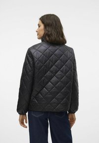 Giubbotto imbottito nero con colletto alto, caratterizzato da motivi a diamante e polsini elasticizzati. Il materiale ha una texture liscia e lucida.