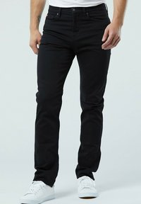 Jean en denim noir avec une coupe slim, comportant cinq poches, une fermeture à bouton sur le devant, et des baskets blanches. Texture lisse et sans motifs.