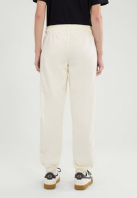 Weiße Jogginghose mit elastischem Bund und gerippten Bündchen, kombiniert mit weißen Sneakers mit schwarzen und braunen Akzenten.