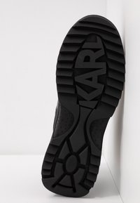 Semelle de chaussure noire avec des rainures profondes et des motifs texturés, présentant le nom de la marque "KARL" en relief de manière bien visible sur la bande de roulement.
