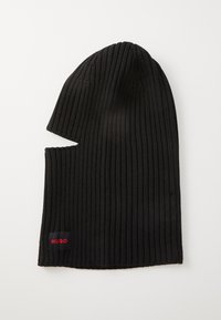 Gorro negro de canalé con un diseño alargado y un corte lateral. Presenta una pequeña etiqueta roja "HUGO" cosida cerca del dobladillo.