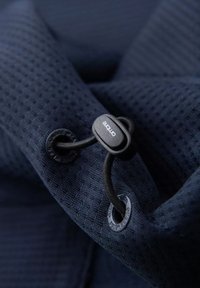 Marinblått textured tyg med ett nätmönster, med en svart dragsträng och logotyp-märkt lås. Inkluderar runda öglor för säker fastsättning.