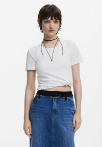Vit, kortärmad, figursydd t-shirt som är snodd i midjan, paired med en högmidjad, knälång, mörkblå denimkjol med fransar.