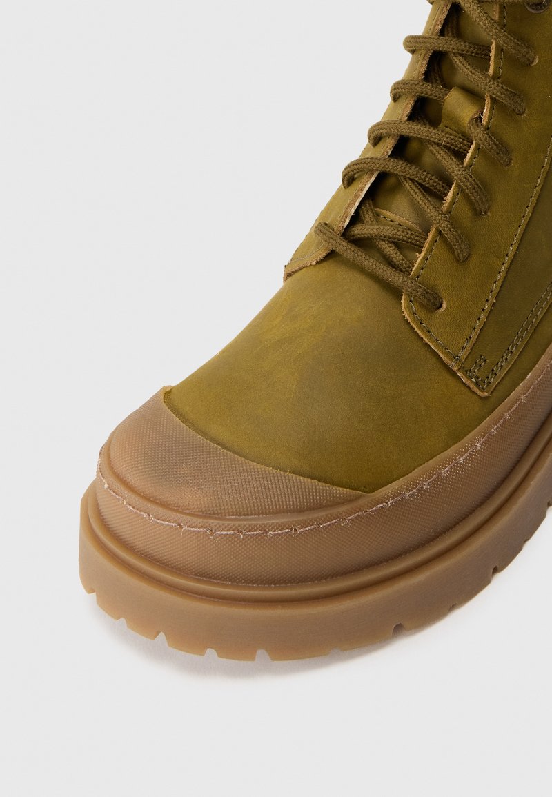 Olive green leather high-top sneaker with round toe, fabric accents, tonal laces, and translucent rubber sole featuring gripped texture.