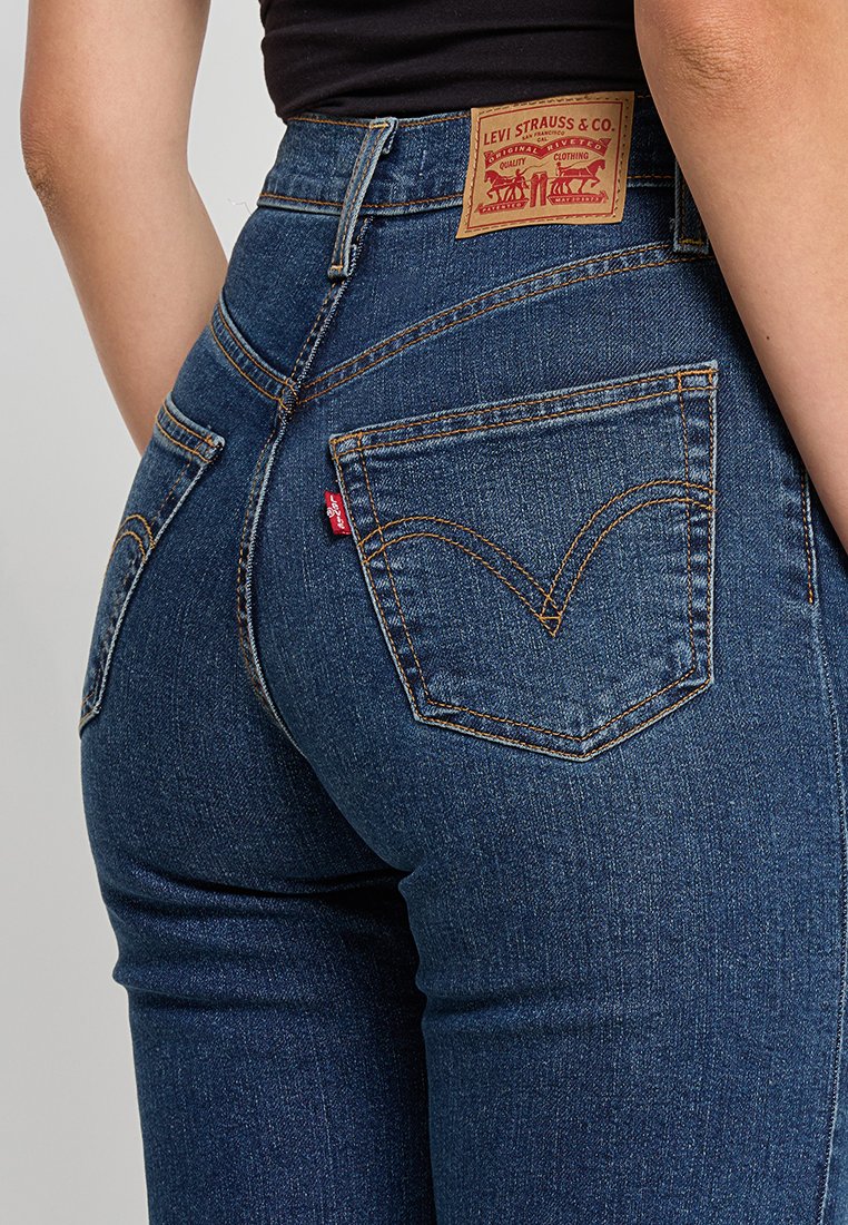 Jeans in denim blu scuro con vita alta, dotati di due tasche posteriori e una patch in pelle con il logo del marchio sulla cintura.