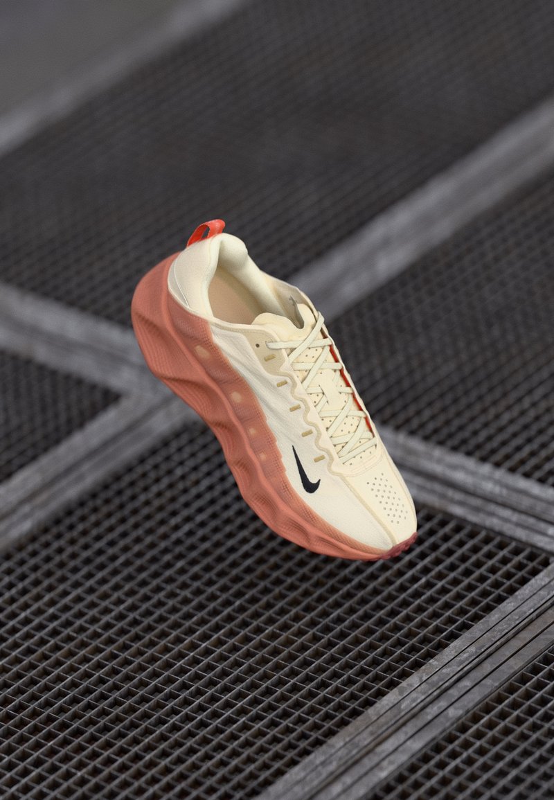 Nike sneaker featuring a cream upper, red accents, lacing system, textured sole, and a logo on the side, presented against a grid background.