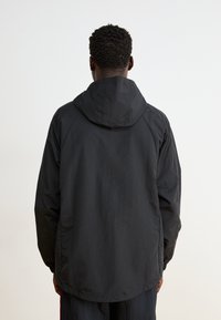 Black hooded jacket with a lightweight, smooth texture, featuring long sleeves and a relaxed fit. Simple design, no visible patterns or accents.