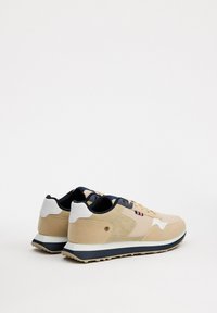 Zapatillas deportivas beige de ante y malla, con detalles en blanco y azul marino, que presentan una suela moldeada y un logo decorativo en el lateral.