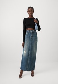 Črna dolga majica s dolgimi rokavi, kombinirana z visokim pasom in raztrganim denim krilom maxi, ki ima bledikave modre odtenke in raven silhueto.