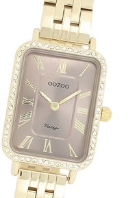 Montre rectangulaire dorée avec un cadran en cristal, un cadran marron avec des chiffres romains et un bracelet en maillons métalliques. Nom de la marque : OOZOO.