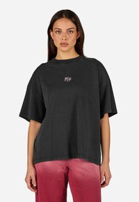 T-shirt oversized preta feita de algodão, apresentando um pequeno logotipo roxo no peito e um corte descontraído com mangas curtas.