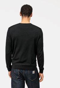 Zwarte crewneck trui met gestructureerde schouders, aangesloten manchetten en een geribbelde zoom. Gecombineerd met donkere denim jeans met contrasterende stiksels.