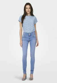 Lyseblå kortærmet top med mønstrede udskæringer, parret med højtaljede lyseblå skinny jeans og blå hæle.