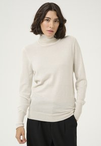 Hellbeige Rollkragenpullover mit langen Ärmeln, weichem Material, figurbetontem Schnitt und Rippstrickdetails an den Bündchen und dem Saum.