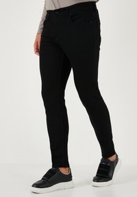 Svarta denimjeans med slim fit, femficksdesign, framknäppning med knapp och kontrasterande sömmar, tillsammans med svarta sneakers.