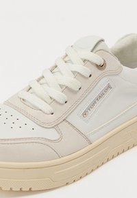 Light-colored sneaker with a smooth leather and suede upper. Features round white laces, perforations on the toe, and a textured sole.