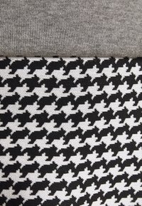 Tissu tricoté gris plié sur un textile à motif pied-de-poule noir et blanc.