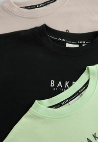 Three T-majice v črni, svetlo rožnati in metino zeleni barvi, z okroglo ovratnikom in imenom blagovne znamke "BAKER by TED BAKER" natisnjenim v belem.