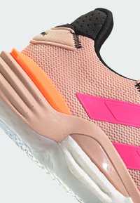 Svetloružová športová obuv s mriežkovaným zvrškom, čiernymi akcentmi, oranžovým detailom na päte a fialovými bočnými pruhmi. Štruktúrovaná podrážka s priehľadnými časťami.
