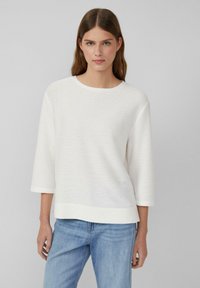Witte, textuurgevers lange mouwen top met een ronde hals. De stof heeft subtiele horizontale strepen en een relaxte pasvorm, gecombineerd met blauwe jeans.