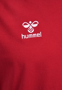 Rode katoenen T-shirt met een witte geborduurde logo met een vlinderontwerp en de tekst "hummel" eronder. Vriendelijke textuur.