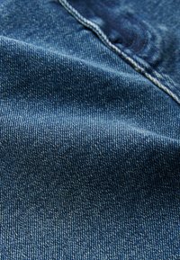 Dunkelblaue Denim-Stoff mit glatter Textur, sichtbaren Nähten und einem subtilen Glanz, der das Webmuster hervorhebt.