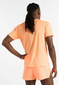Short-sleeve, breathable athletic shirt and shorts in bright orange with a textured pattern; features side slits for increased mobility.