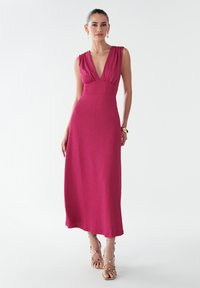 Fuchsia maxi dress with a plunging V-neck, sleeveless design, and gathered detail at shoulders, made from textured fabric.