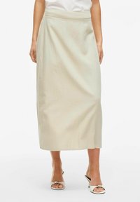 Jupe maxi en lin beige clair avec une coupe évasée et une large taille, présentant une texture lisse et une conception qui descend jusqu'au sol.