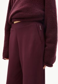 Burgunderfarbene, weit geschnittene Hosen mit Seitentaschen, aus weichem, strukturiertem Stoff. Kombiniert mit einem passenden, flauschigen Pullover.