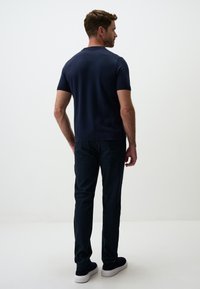 Granatowa koszula z krótkim rękawem, dopasowany krój, mieszanka bawełny. Połączona z ciemnymi spodniami i czarnymi sneakersami. Prosta, klasyczna sylwetka bez wzorów.