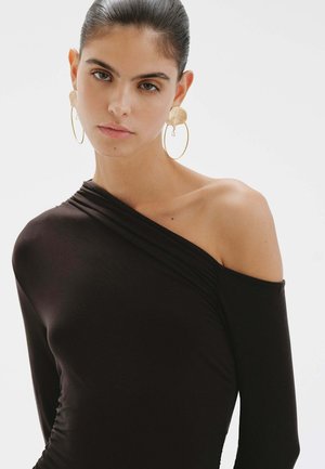 Top negro con los hombros al descubierto, con detalle fruncido, diseño ajustado y textura suave. La modelo lleva unos grandes pendientes de aro dorados.