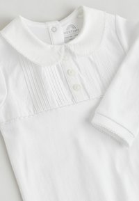 Biały bodysuit dla niemowląt z okrągłym kołnierzykiem, detalami z fałdami, z pięcioma guzikami oraz falbanką na rękawach i kołnierzyku.