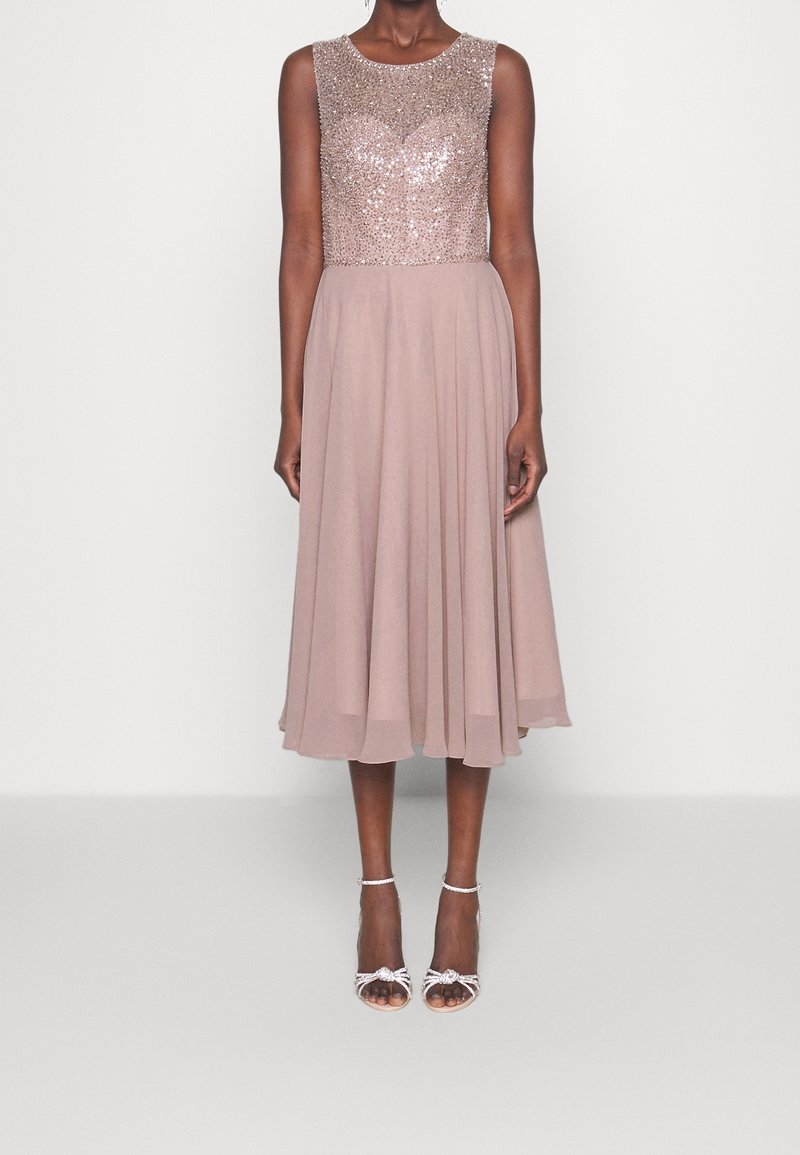 Klänning med pärlbroderad överdel, en topp med nakna paljetter och en flytande chiffongkjol till knälängd. Kombinerad med ljusa, remmade klackskor.