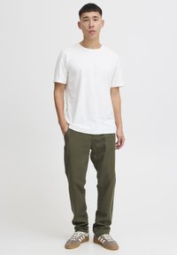 Hvit t-skjorte med korte ermer kombinert med olivengrønne bukser og grå joggesko med hvite striper. Enkelt, rent design med en avslappet passform.