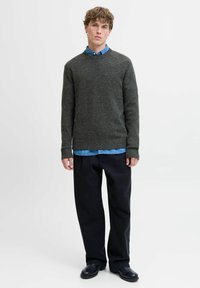 Pull en maille gris foncé avec un col rond, porté sur une chemise col bleu, associé à un pantalon noir et des chaussures noires.