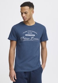 Karinė mėlyna medvilninė marškinėliai su apykakle, ant kurių yra balti grafikos užrašai „Reikalauk savo teisių“ ir „Vintage Denim“ kreivuoju dizainu.