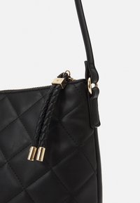 Musta tikattu nahkalaukku, jossa punottu olkahihna, kullanväriset metalliosat ja vetoketjullinen suljin, pehmeä ja teksturoitu pinta.