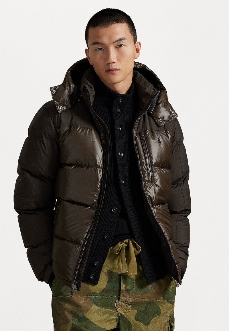 Brown puffy jacket with a shiny, quilted finish and detachable hood, layered over a black knit sweater, paired with camo cargo pants.