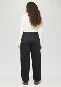 Hoch taillierte schwarze weite Jeans mit strukturiertem Finish. Verfügt über zwei Gesäßtaschen und wird mit einem langärmeligen weißen Shirt kombiniert.