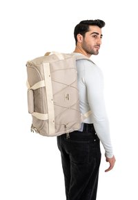 Zaino beige realizzato in tessuto testurizzato, con spallacci bianchi, una tasca frontale con zip e un dettaglio con corda bungee per ulteriore spazio di stoccaggio.