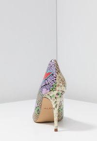 Chaussure à talon aiguille avec un motif en cuir de serpent coloré, présentant des teintes de violet, vert, rouge et beige, vue de l'arrière sur une surface blanche.