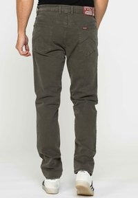 Jeans tapered da uomo di colore verde oliva con finitura testurizzata, dotati di due tasche posteriori e un etichetta con il marchio in vita.