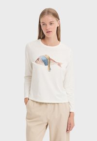 Long-sleeve white T-shirt featuring a colorful fish graphic with a blue headscarf. Soft fabric and relaxed fit. Worn with beige pants.