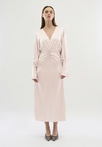 Rochie cu mâneci lungi și guler în V, din satin moale de culoare roz pal, cu detalii pliate la talie și manșete evazate. Pur tată cu tocuri ascuțite și strălucitoare.