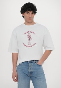 Hvit oversized t-skjorte med rødt grafisk trykk som viser en figur og teksten "Fiorucci 1967 dreaming of you." Myk bomullsmateriale.