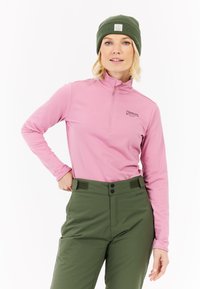 Šviesiai rožinė ilgomis rankovėmis, ketvirtį užtrauktuku užsegama palaidinė su logotipu ant krūtinės, derinama su žaliais aukštai liemeniui priglundančiais džinsais, kuriuose yra mygtuko ir Velcro užsegimai.