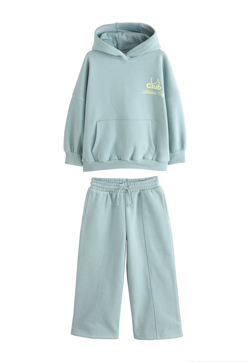 Vaaleansininen huppari ja siihen sopivat collegehousut, valmistettu pehmeästä kankaasta. Hupparissa on etutasku ja rinnan kohdalla kirjailtu teksti.