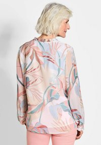 Langärmlige Bluse aus leichtem Stoff mit einem pastellfarbenen Blumenmuster in den Farben Pink, Blau und grünen Blättern; geraffter Ausschnitt und Bündchen.